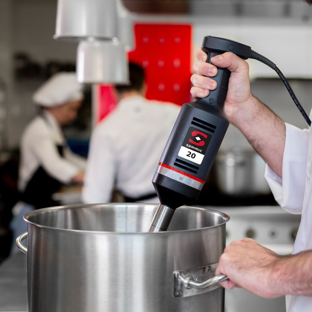 Chef utilizando el batidor de mano profesional Sammic XM-22 en una cocina industrial, mezclando ingredientes en una olla de gran capacidad.