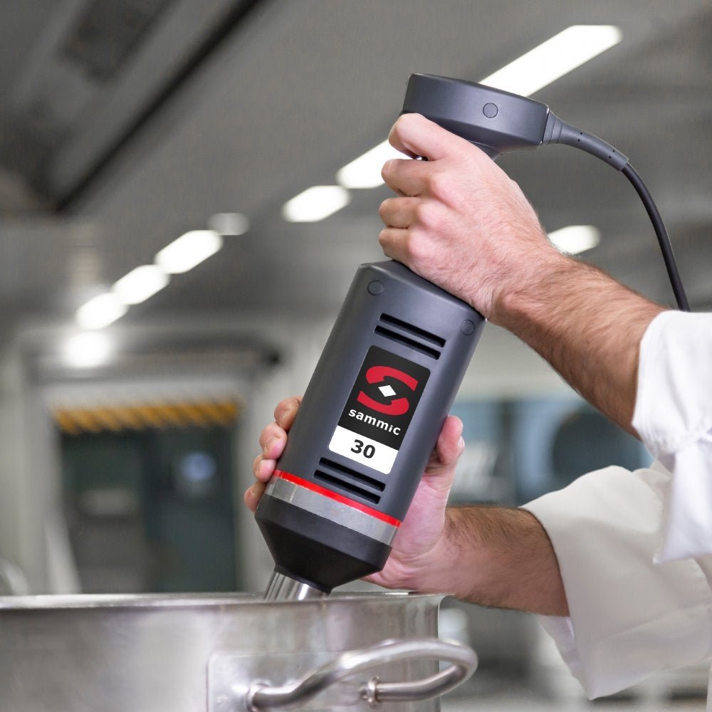Chef utilizando el batidor de mano profesional Sammic XM-31 en una cocina industrial, ideal para la mezcla y emulsión de grandes volúmenes de ingredientes.