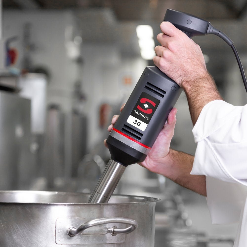 Chef utilizando el batidor de mano profesional Sammic XM-33 en una cocina industrial, mezclando ingredientes con precisión en una olla de gran capacidad.